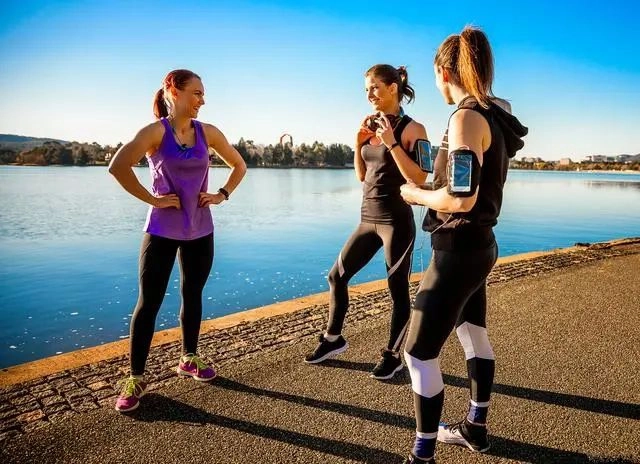 Three women warm up by the river, ready for aerobic exercise