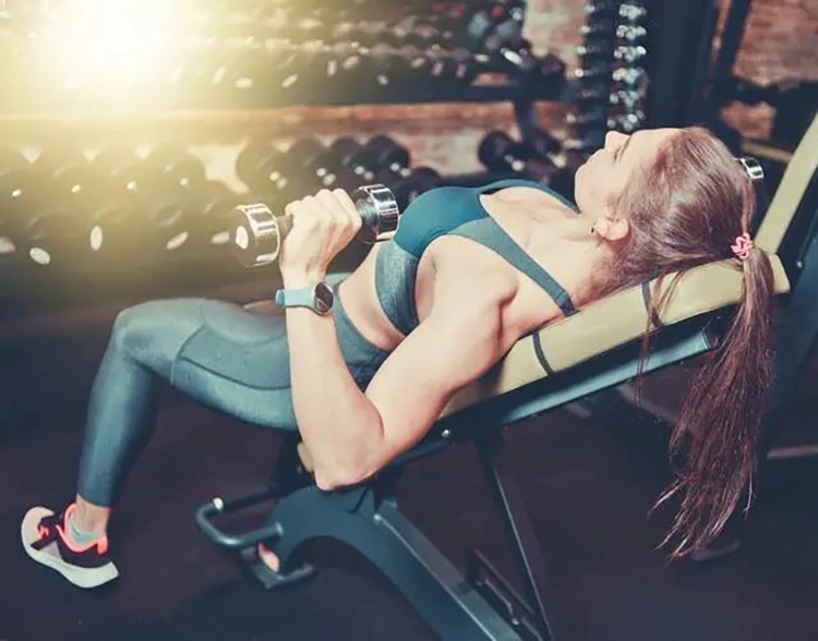 She bench presses with little dumbbells at the gym, doing anaerobic exercises