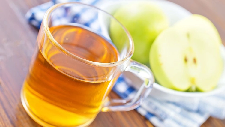 A large glass of vegetable oil and a cut green apple.