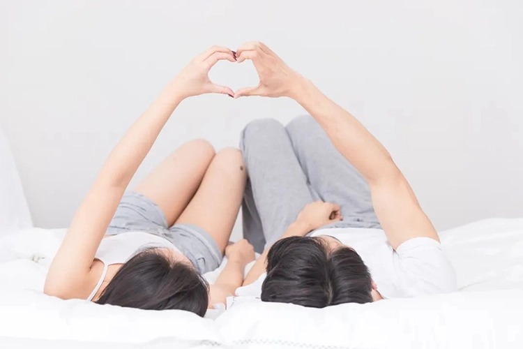 Couples lie on the bed and make a heart shape with their hands