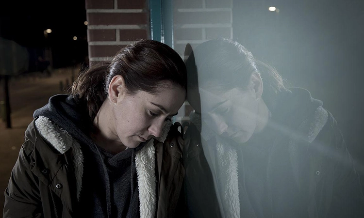 The sad and depressed person leans against the window of the street at night