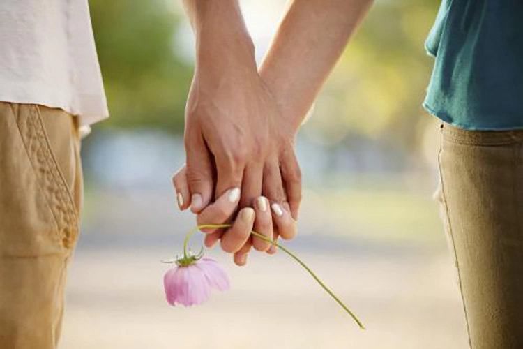 They hold hands and hold a bouquet of flowers