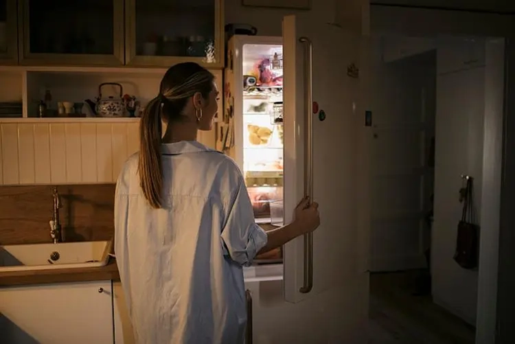 The young woman looked for food in the refrigerator at night.