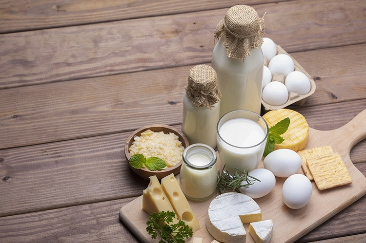 There are milk, eggs and cheese on the wooden table.