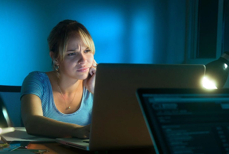 A disappointed and frustrated woman works on the computer at night