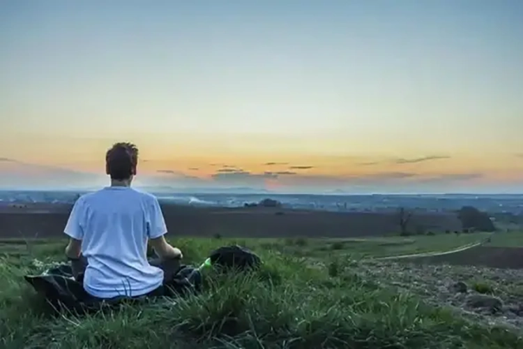 He is doing mindfulness meditation on the grass