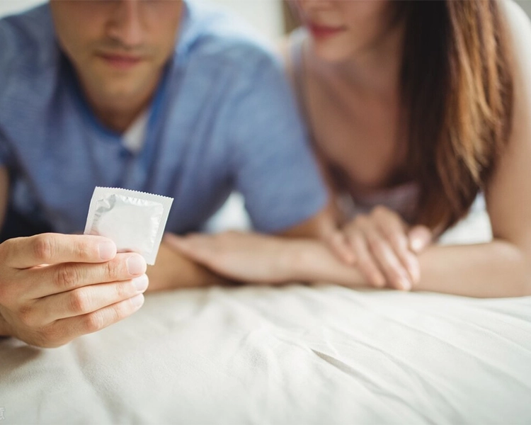 The couple lies on the bed with a condom.