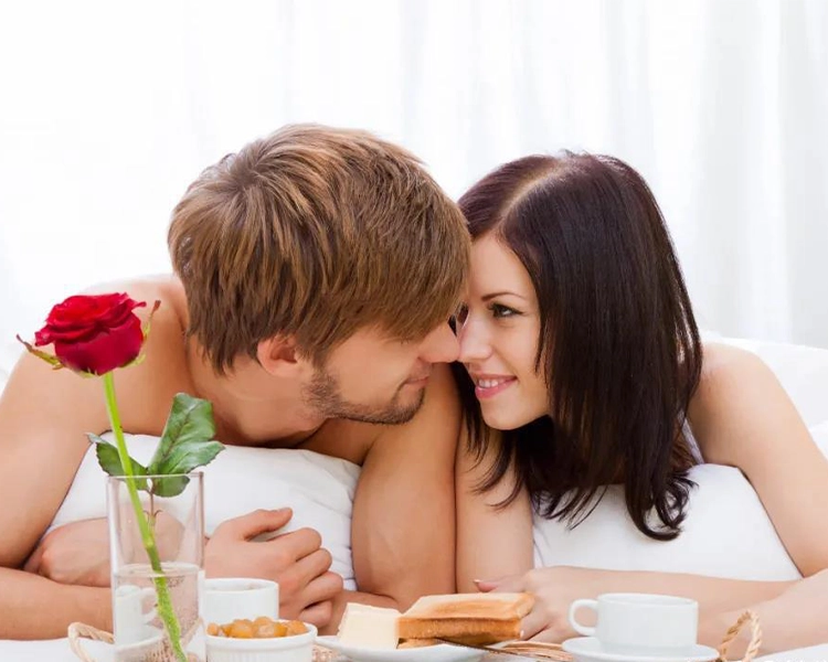 The couple's noses are touching in bed, and they look very affectionate.