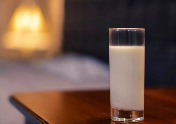 There is a glass of milk on the wooden table by the window.