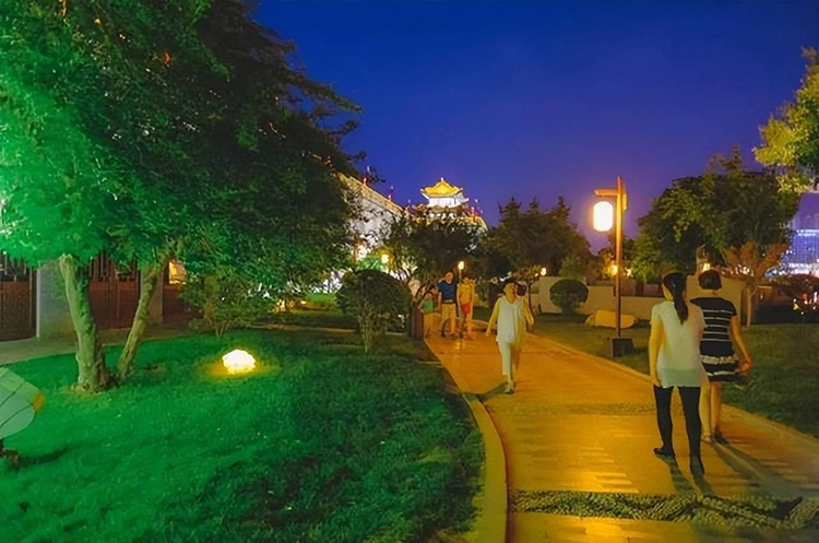 There are many people walking in the park at night.