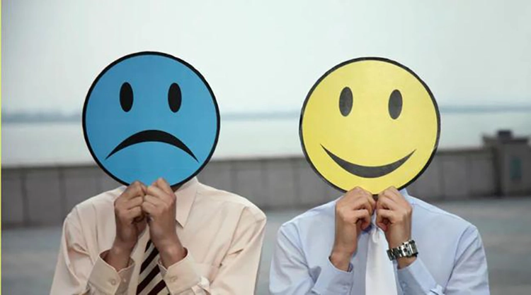 Dos personas sostienen una cara sonriente y una cara llorando para expresar emociones.